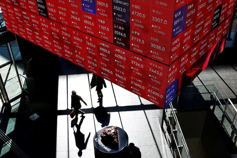 Visitors walk under Japan"s Nikkei stock prices quotation board inside a building in Tokyo on February 16, 2024. Japanese stock prices are within sight of a historic peak reached during the nation"s economic heyday in 1989 as global investors return in droves.