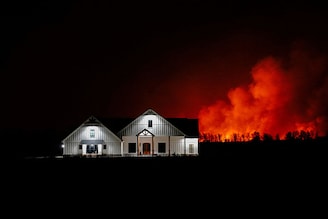 A wildfire that prompted evacuations burns in the distance behind a home outside of Shattuck, Oklahoma, US, February 27, 2024.