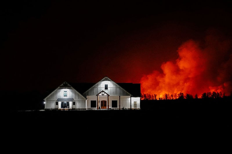 A wildfire that prompted evacuations burns in the distance behind a home outside of Shattuck, Oklahoma, US, February 27, 2024.