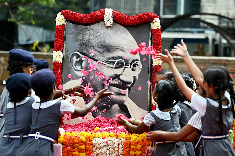 Indian school children throw rose flower petals over a portrait of Mahatma Gandhi to pay their tribute on the death anniversary of the Indian founding father in Chennai on January 30, 2024. The death anniversary of Gandhi, who is widely known in India as Bapu (father), is also observed as Martyrs" Day in the country.