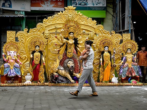 A woman carrying an infant walks past an idol of goddess Durga outside a workshop in Kumartoli, Kolkata, on July 16, 2024, before it is exported to Texas state in the US ahead of Durga Puja.