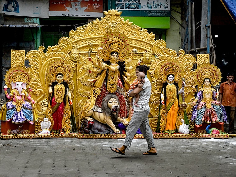 A woman carrying an infant walks past an idol of goddess Durga outside a workshop in Kumartoli, Kolkata, on July 16, 2024, before it is exported to Texas state in the US ahead of Durga Puja.