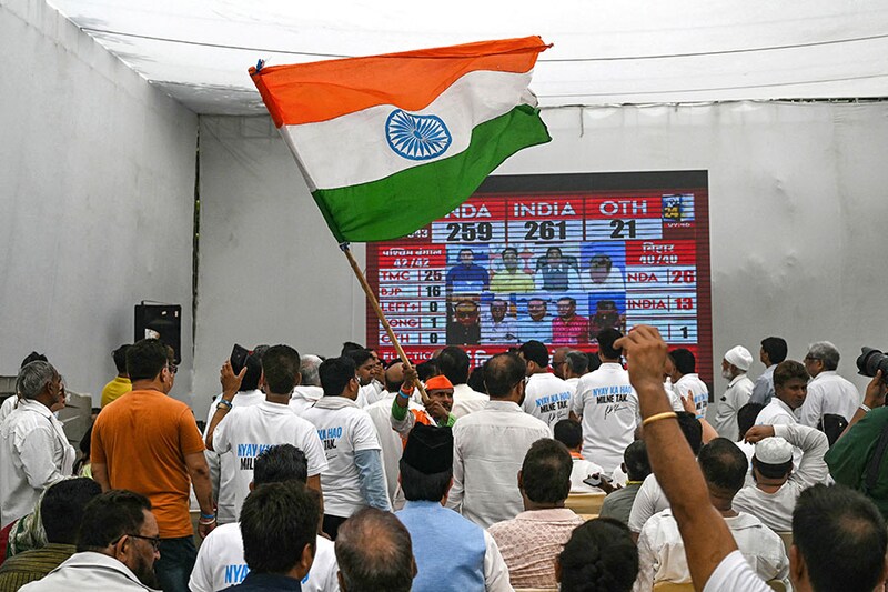 A supporter of the Indian National Congress (INC) party waves India"s national flag as others watch live election results displayed on a television after the counting of votes began for the country"s general election at the INC headquarters in New Delhi on June 4, 2024.