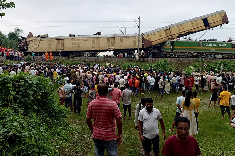 People look on at the site of a collision between an express passenger train and a goods train in Nirmaljote, near Rangapani station in West Bengal, on June 17, 2024. At least seven people were killed when the trains collided, derailing three passenger carriages, police said.