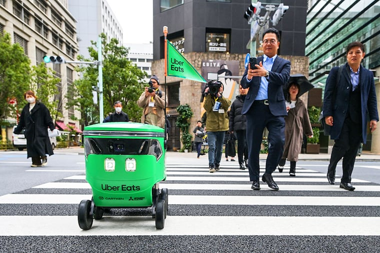 Members of the media and passersby walk next to an unmanned robot as it crosses the street during a demonstration of a robot delivery service by Uber Eats Japan, Mitsubishi Electric and robot developer Cartken in downtown Tokyo on March 5, 2024.