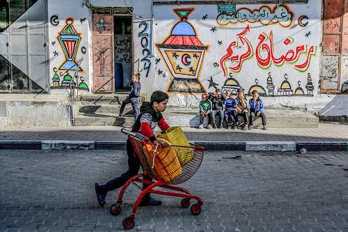 A Palestinian child pushes a cart containing water jerrycans in front of a wall bearing Ramadan theme drawings in Gaza city amid the ongoing conflict between Israel and Hamas militants, as Muslim worshippers prepare to welcome the holy fasting month of Ramadan, which begins next week. Image: AFP