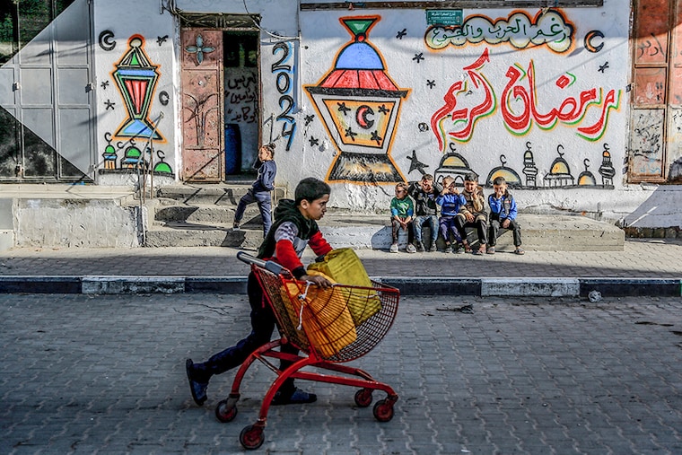 A Palestinian child pushes a cart containing water jerrycans in front of a wall bearing Ramadan theme drawings in Gaza city amid the ongoing conflict between Israel and Hamas militants, as Muslim worshippers prepare to welcome the holy fasting month of Ramadan, which begins next week. Image: AFP