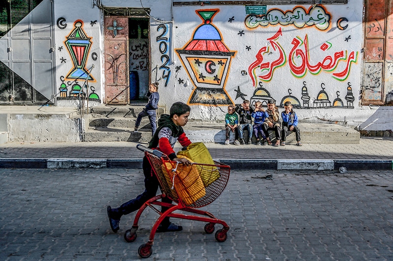 A Palestinian child pushes a cart containing water jerrycans in front of a wall bearing Ramadan theme drawings in Gaza city amid the ongoing conflict between Israel and Hamas militants, as Muslim worshippers prepare to welcome the holy fasting month of Ramadan, which begins next week. Image: AFP