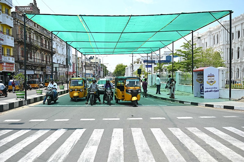 Commuters at a zebra crossing wait beneath a temporary shelter to beat the heat on a hot summer day in Chennai on May 9, 2024.
