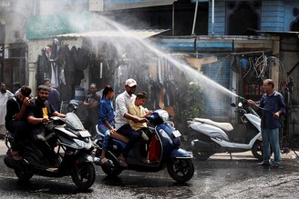 People on their scooters pass under a water sprinkler on a hot summer day in Ahmedabad, India, May 9, 2024.