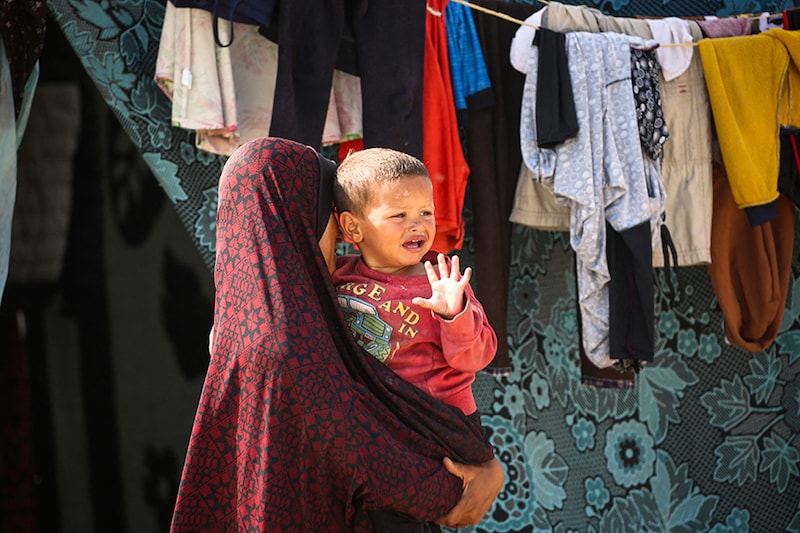 A displaced Palestinian carries her son at a temporary camp in Rafah on May 17, 2024, amid the ongoing conflict between Israel and the militant group Hamas.