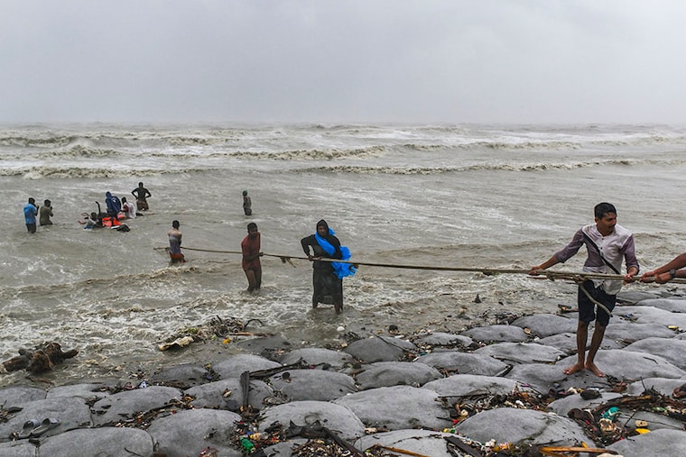 People try to rescue a tractor in heavy sea waves and strong wind during the landfall of Cyclone Remal at a beach in Kuakata, Bangladesh, on May 27, 2024. Residents of low-lying coastal areas of Bangladesh and India survey the damage as an intense cyclone weakens into a heavy storm, with at least two people dead, roofs ripped off, and trees uprooted.