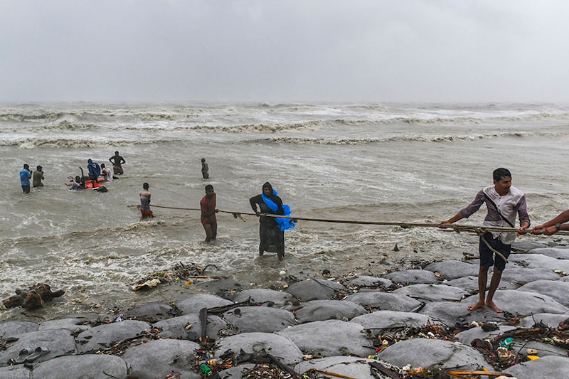 People try to rescue a tractor in heavy sea waves and strong wind during the landfall of Cyclone Remal at a beach in Kuakata, Bangladesh, on May 27, 2024. Residents of low-lying coastal areas of Bangladesh and India survey the damage as an intense cyclone weakens into a heavy storm, with at least two people dead, roofs ripped off, and trees uprooted.