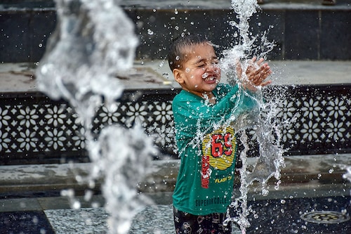 A boy seen cooling off with fountain water on a scorching summer day. Kashmir valley experienced a significant rise in temperatures with several areas recording the highest temperatures in decades. The Meteorological Department predicted the continuation of the heatwave in the next month too. (Photo by Saqib Majeed/SOPA Images/LightRocket via Getty Images)