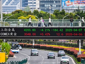 People walk across a bridge with a stock"s indicator board in the financial district of Shanghai on April 7, 2025. Asian equities collapsed on a black Monday for markets after China hammered the United States with its own hefty tariffs, ramping up a trade war many fear could spark a recession.