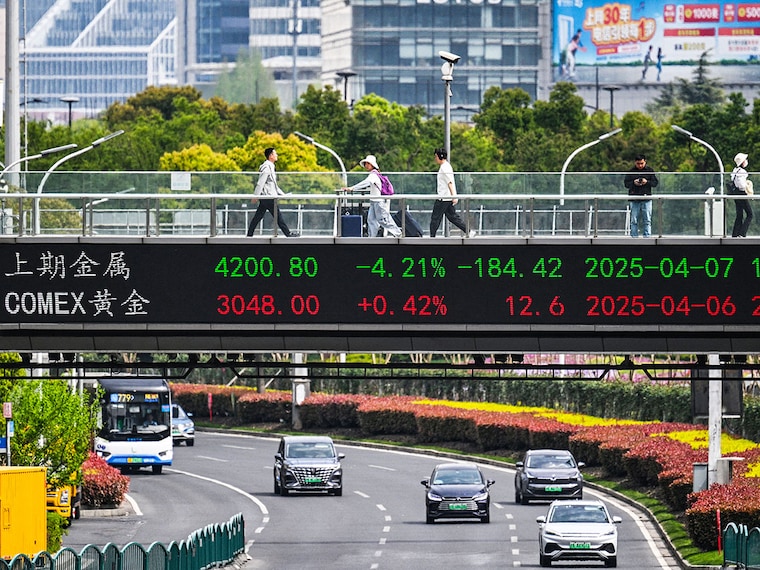People walk across a bridge with a stock"s indicator board in the financial district of Shanghai on April 7, 2025. Asian equities collapsed on a black Monday for markets after China hammered the United States with its own hefty tariffs, ramping up a trade war many fear could spark a recession.