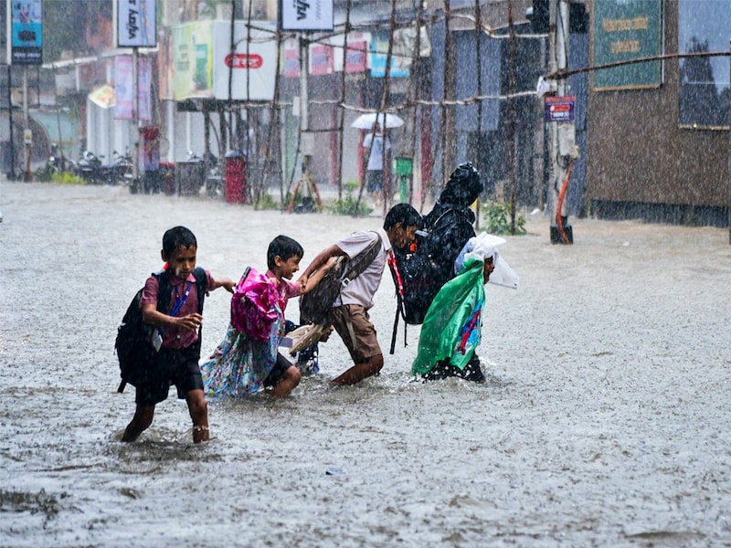 Children wade through a waterlogged road following heavy rainfall, in Mumbai, Monday, August 18, 2025.