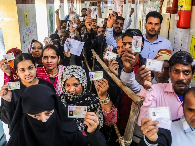 Voters show their ID cards as they wait in queues at a polling booth to cast votes during the Delhi Assembly elections at Shahzada Bagh in New Delhi on Wednesday, February 5, 2025.