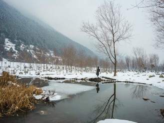 A man stands near a partially frozen pond, next to a tree, on a chilly day in Ganderbal, Jammu & Kashmir on 4th January, 2025. The India Meteorological Department (IMD) has forecasted heavy snowfall in Jammu and Kashmir on Saturday and Sunday, accompanied by light to moderate rainfall in the nearby plains. The heaviest snowfall is expected from Saturday night to Monday morning.