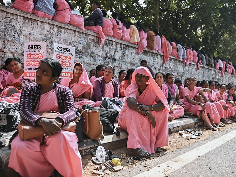 Karnataka"s Accredited Social Health Activist (ASHA) workers sit on a road on January 7, 2025, as they take part in an indefinite protest at Freedom Park in Bengaluru, demanding a hike in honorarium payment and immediate disbursal of three months" worth of pending dues.