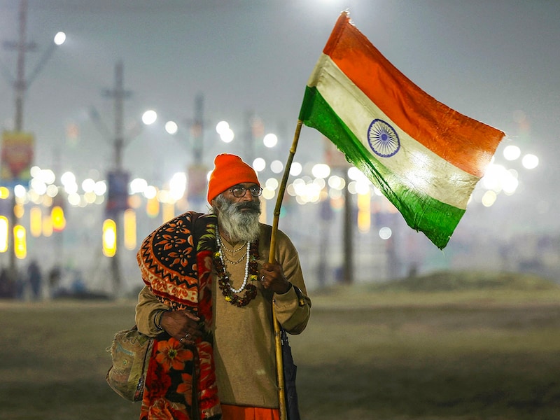 A Hindu pilgrim stands with the Indian national flag during the Maha Kumbh Mela festival near Sangam, the confluence of the Ganges, Yamuna, and mythical Saraswati rivers, in Prayagraj on January 16, 2025. Vast crowds of Hindu pilgrims are expected to assemble over six weeks for the festival, which is the world"s largest gathering of humanity. Organisers expect 400 million people to attend.