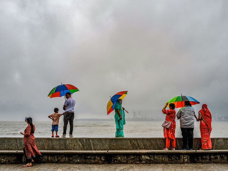 People stand at seafront as it rains in Mumbai on June 18, 2025.