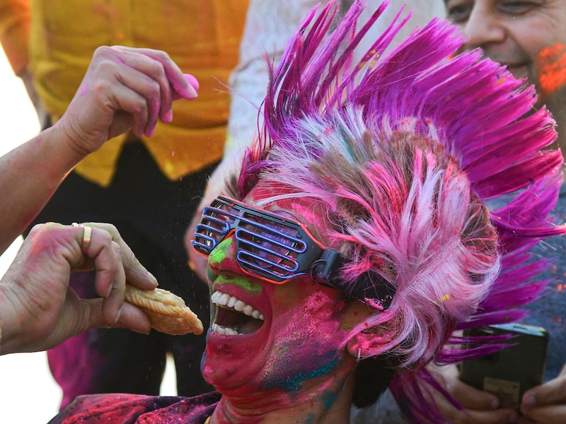 A Holi reveller smeared in colours is offered gujiya, a traditional Indian sweet associated with Holi, the spring festival of colours, in Chandigarh on March 14, 2025.