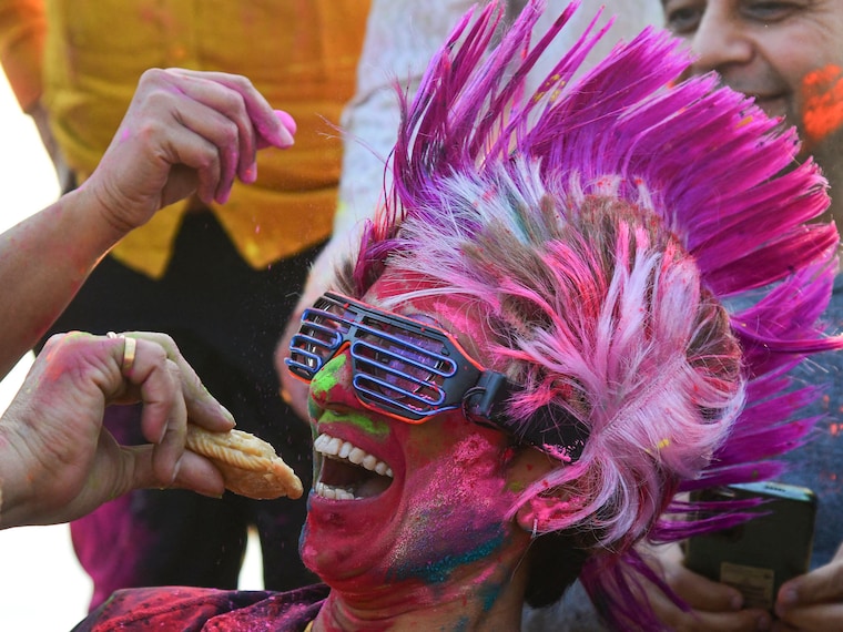 A Holi reveller smeared in colours is offered gujiya, a traditional Indian sweet associated with Holi, the spring festival of colours, in Chandigarh on March 14, 2025.