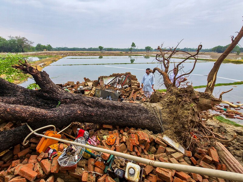 People stand near the debris of a house after a tree fell on it following strong gusty winds that accompanied rains in the city, causing it to collapse, at Najafgarh area, in New Delhi, Friday, May 2, 2025.