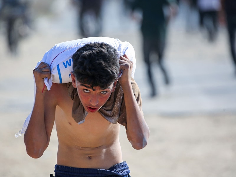 A displaced Palestinian youth ferries a bag of food aid on his shoulders after people stormed a World Food Programme warehouse in Deir el-Balah in the central Gaza Strip on May 28, 2025. The United Nations on May 28 condemned a US-backed aid system in Gaza following a chaotic food distribution where 47 people were injured, after Israel allowed supplies in at a trickle last week, easing a full blockade imposed on the besieged Palestinian territory for over two months.