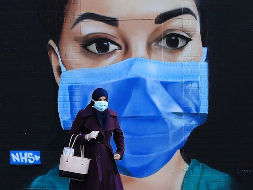  <p>LONDON,      ENGLAND: A woman wearing a face mask walks past a piece of  street art      depicting an NHS worker in the Shoreditch area</p>