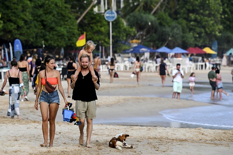 In this picture taken on March 25, 2022, tourists walk along a beach in Mirissa, a small town on the south coast of Sri Lanka. Tourism became crucial to the economy — its pandemic-enforced closure underlies the foreign exchange shortage that is the root cause of the current situation. (Credit: Ishara S. KODIKARA / AFP)