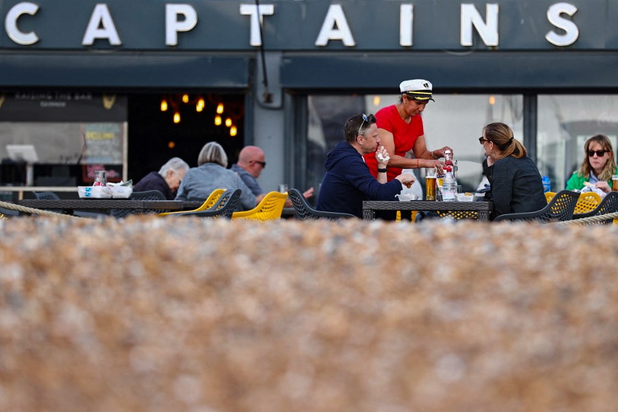 Fish and Chip shop owner Pam Sandhu (4R) serves customers as they sit and eat lunch outside of Captain's Fish and Chips shop in Brighton on March 25, 2022. Britain's fish and chip shops have weathered the storm of Brexit and Covid, and are fighting the tide of rising inflation but thousands could be sunk by the war in Ukraine. (Credit: ADRIAN DENNIS / AFP)