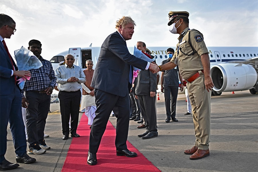 Britain's Prime Minister Boris Johnson (C) is greeted by a police official upon his arrival at the airport in Ahmedabad on April 21, 2022. (Credit: BEN STANSALL / POOL / AFP)