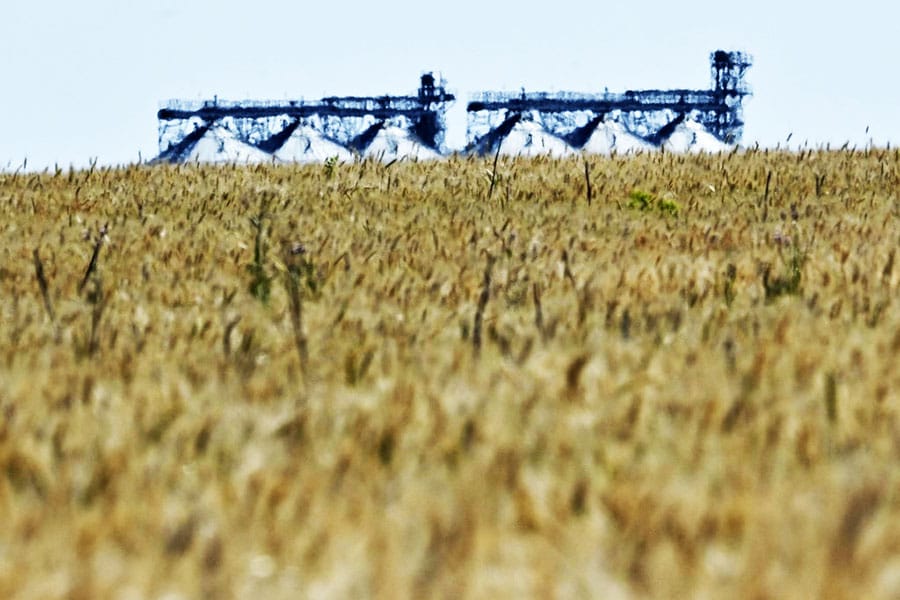 A photograph shows a grain elevator behind a wheat field in Ukraine's eastern region of Donbas, on July 1, 2022, amid Russia's military invasion launched on Ukraine. Between a lack of fuel and the risk of being bombed, some Ukrainian farmers are wondering how they will harvest their fields as the period for certain crops approaches in July. Image: Genya SAVILOV / AFP