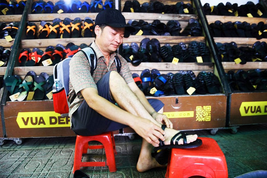 A client trying on rubber sandals at a shop in Hanoi. Image: Nhac Nguyen/ AFP