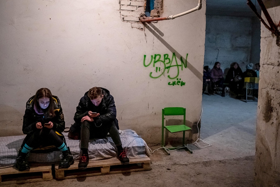 A young couple use their mobile phones as they sit in a school basement which is used as an air-raid shelter, amid Russia's invasion of Ukraine, in Drohobych, Ukraine, March 21, 2022. (Credit: Viacheslav Ratynskyi / Reuters)