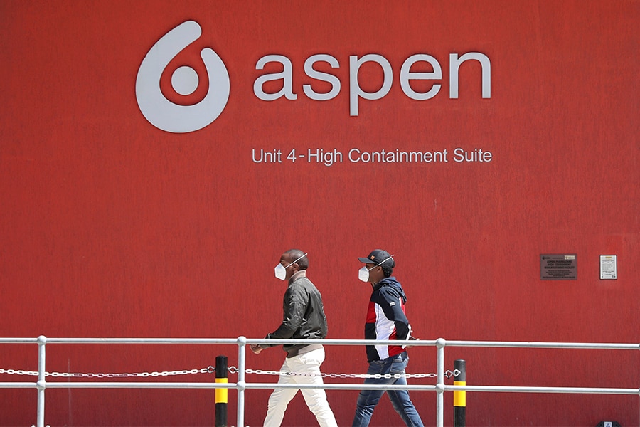 People wearing face masks walk past a logo of South African pharmaceutical major Aspen Pharmacare in Gqeberha. Image: Siphiwe Sibeko​/ Reuters