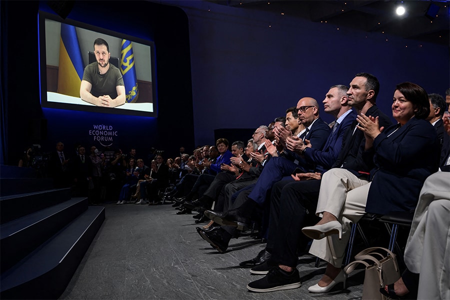 Participants with Permanent representative of Ukraine to the United Nations office in Geneva, Yevheniia Filipenko (R) Ukrainian former boxer Wladimir Klitschko (2nd R) and Kyiv's Mayor Vitali Klitschko (3rd R) applaud the speech of Ukrainian President Volodymyr Zelensky (screen) following his address by video conference during the World Economic Forum (WEF) annual meeting in Davos on May 23, 2022. (Credits: Fabrice COFFRINI / AFP​)