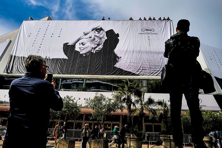 People watch as workers hang the official poster of the 76th Cannes Film Festival featuring a photograph of actress Catherine Deneuve by Jack Garofalo, on the facade of the Palais des Festivals in Cannes, southeastern France, on May 14, 2023. Image: Valery HACHE / AFP