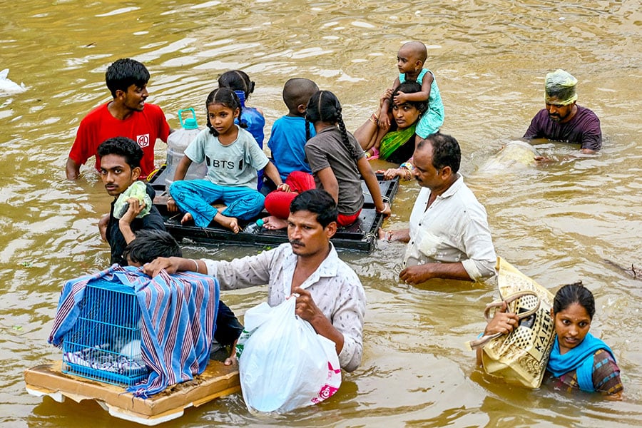 People carry their belongings as they wade through a flooded street after heavy monsoon rains, in Vijayawada on September 2, 2024. - Intense monsoon rains and floods in India's southern states have killed at least 25 people, with thousands rescued and taken to relief camps, disaster officials said on September 2. Image: Changdu Lumburu / AFP 