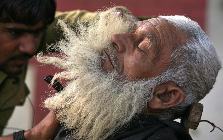 Ahmed Khan, 58, a rickshaw puller, gets his beard dressed by a roadside barber in Noida near New Del