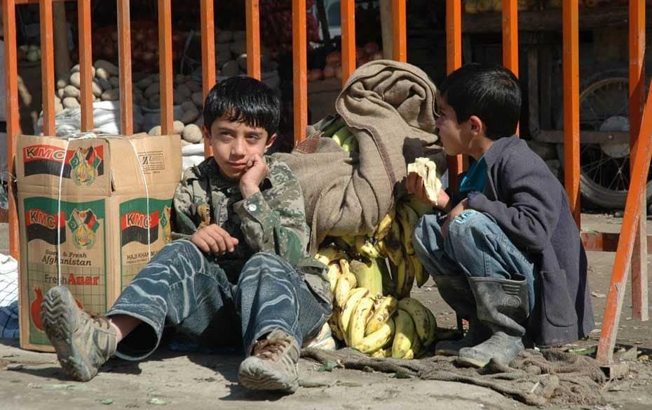 Boys at a vegetable and fruits market. The carton in the picture has pomegranates. Afghan pomegranat