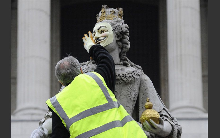 An official removes a mask placed on a statue of Britain's Queen Anne at the 'Occupy' ca