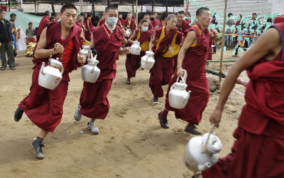 Buddhist monks carrying kettles run towards the complex to serve tea to the devotees attending a tea