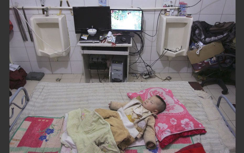 A child sleeps on a bed next to urinals at his home inside an unused toilet of a hotel in Shenyang, 