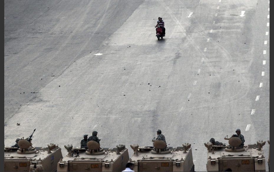 Two men on a scooter ride near soldiers on military vehicles at Abbasiya square near Egypt's Def