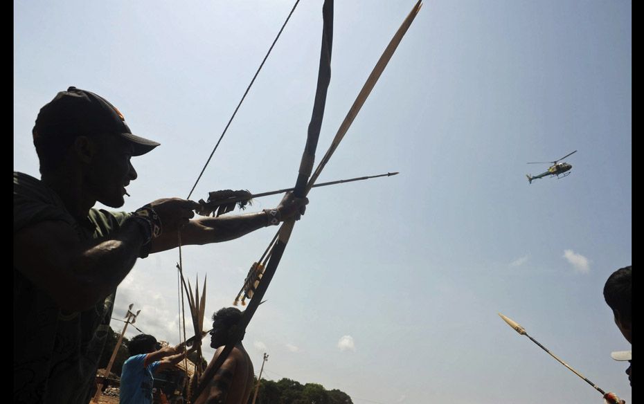 Amazonian Indians, fishermen and local residents react as a helicopter flies over them as they block