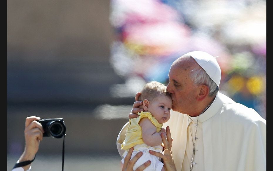 Pope Francis kisses a baby as he arrives to lead the weekly audience in Saint Peter’s Square a