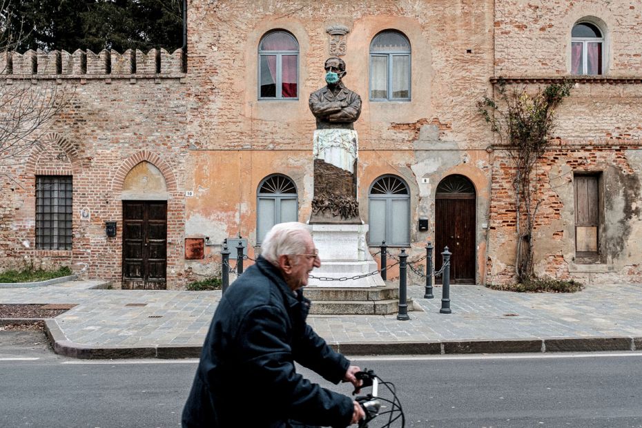 ITALY: A pensioner, not wearing a mask, rides a bicycle past a statue that has had its face covered 